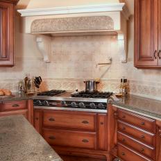 Wood Kitchen Cabinets Surrounding Neutral Covered Range Hood With Small Tile Accent Strip Over Patterned Tile Backsplash
