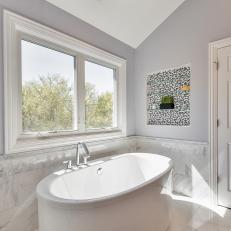 Free Standing Contemporary Bathtub Under Window and Slanted Ceiling With Marble Tile Wall Detailing 