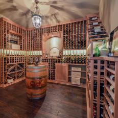 Large Floor to Ceiling Built in Wood Wine Rack in Neutral Wine Cellar With Barrel Table and Traditional Light Fixture 