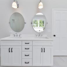 White Contemporary Double Vanity With Unframed Oval Mirrors, Black Cabinet and Drawer Handles and Mounted Sconces