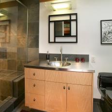 Modern Bathroom With Light Wood Vanity Featuring Stainless Steel Countertop Beside Glass Wall Neutral Tile Shower