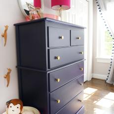 Girl's Bedroom With Navy Wooden Dresser and Hot Pink Table Lamp