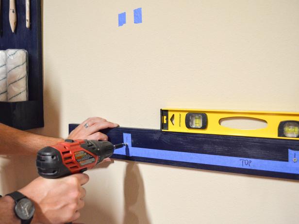 person attaching scrap wood to wall with a drill