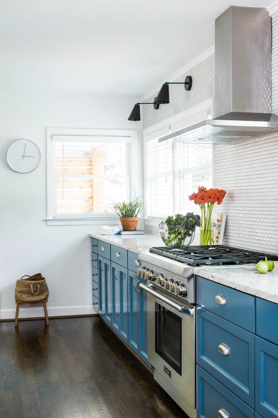 Modern White and Blue Kitchen with Metal Vent Hood, Tile Backsplash and Simple Sconces and Clock