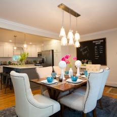 Neutral Fabric Dining Chairs Surround a Wood Table Below a Focal Pendant Chandelier 
