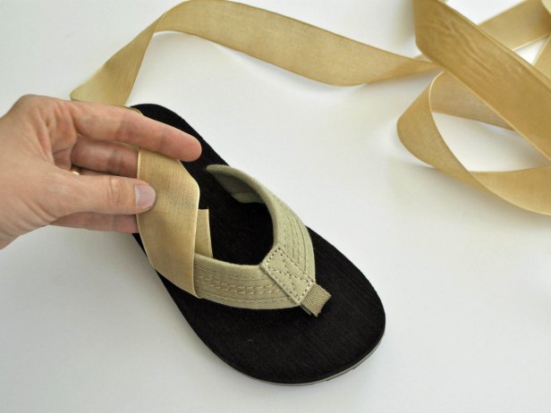 Cut spool of ribbon into four equal parts. Wrap ribbon around flip flop strap and glue as shown. Repeat on other side of flip flop so there are two straps on each sandal. Repeat on other flip flop. Lace shoes up the leg. Tie in a knot and tuck in edges of ribbon.