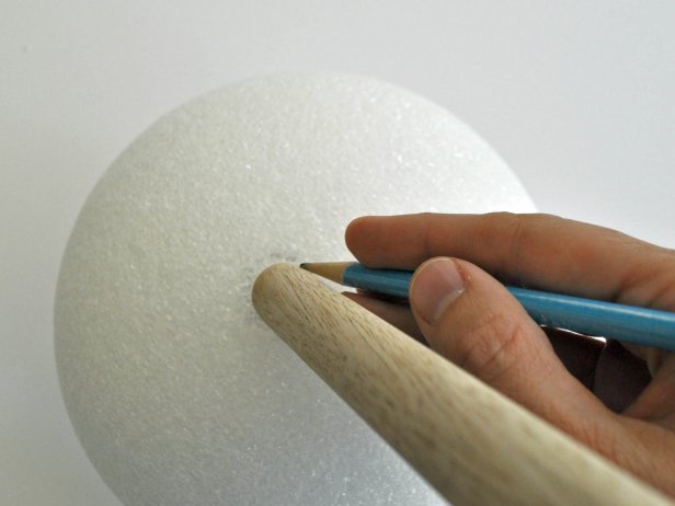 Align wooden dowel onto foam ball and trace around dowel with pencil. Use knife to carve out circular shape 1 inch deep. Hot glue end of dowel and place into hole of foam ball. Add additional glue to fill in around edges of hole. Repeat steps on other foam ball. Tip: Use coolest setting on hot glue gun to void melting foam. Paint barbell with black acrylic paint. Tip: Due to the porous nature of the foam ball, pour paint onto ball, then gently brush it around to coat all textured areas. Do not attempt to use spray paint; spray paint melts foam.