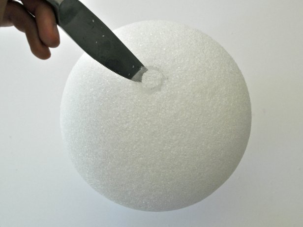 Align wooden dowel onto foam ball and trace around dowel with pencil. Use knife to carve out circular shape 1 inch deep. Hot glue end of dowel and place into hole of foam ball. Add additional glue to fill in around edges of hole. Repeat steps on other foam ball. Tip: Use coolest setting on hot glue gun to void melting foam. Paint barbell with black acrylic paint. Tip: Due to the porous nature of the foam ball, pour paint onto ball, then gently brush it around to coat all textured areas. Do not attempt to use spray paint; spray paint melts foam.