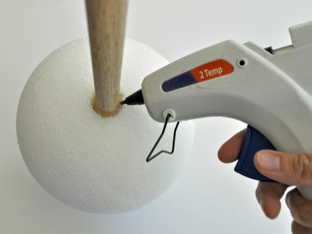 Align wooden dowel onto foam ball and trace around dowel with pencil. Use knife to carve out circular shape 1 inch deep. Hot glue end of dowel and place into hole of foam ball. Add additional glue to fill in around edges of hole. Repeat steps on other foam ball. Tip: Use coolest setting on hot glue gun to void melting foam. Paint barbell with black acrylic paint. Tip: Due to the porous nature of the foam ball, pour paint onto ball, then gently brush it around to coat all textured areas. Do not attempt to use spray paint; spray paint melts foam.
