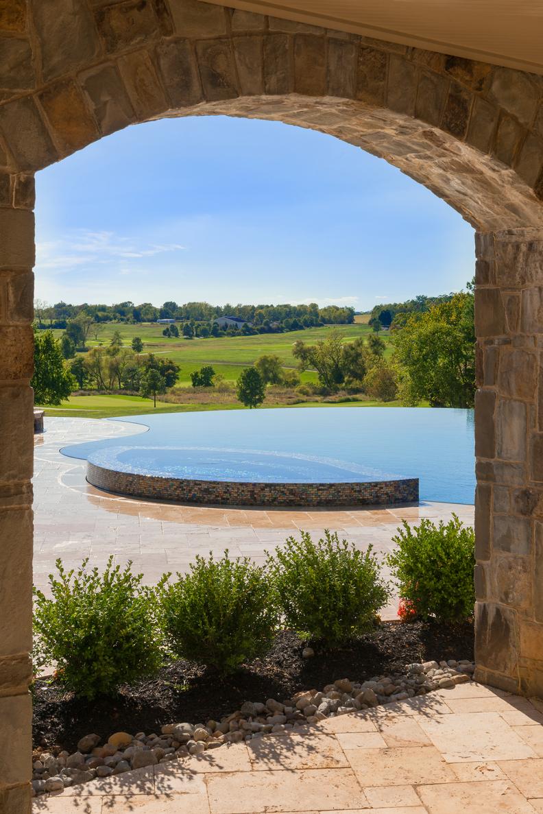 Arched Stone Wall Frames Infinity Pool, Spa and Landscape