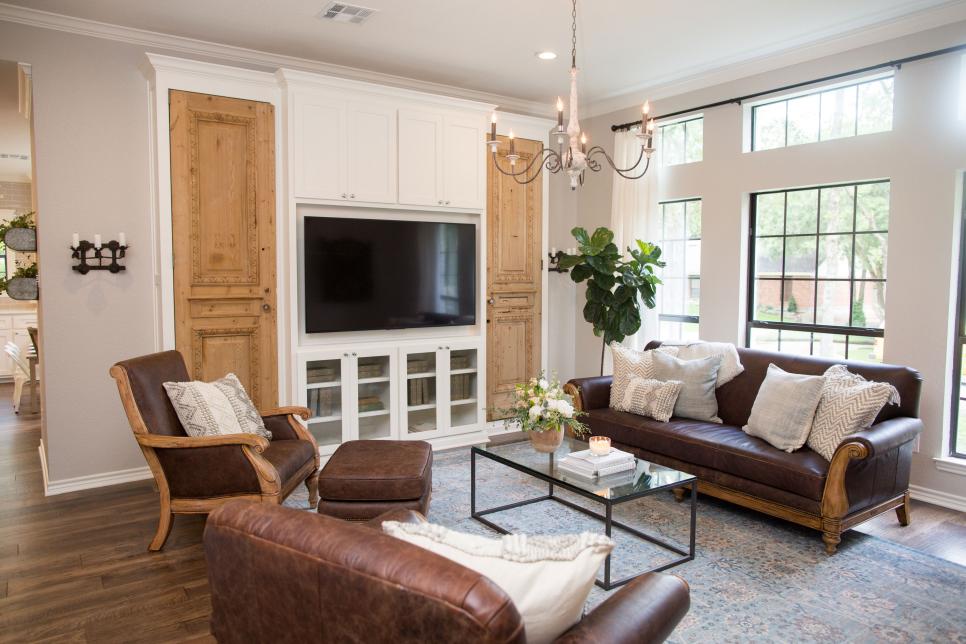 A beautiful living room from Fixer Upper with brown leather furniture and antique style doors flanking the builtins and TV. Come find out the answer to: What Home Improvement Shows are Most Popular in the USA?