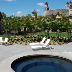 Concrete Rim Hot Tub Over Concrete Backyard Patio With White Lounge Chairs and Organized Shrubs 