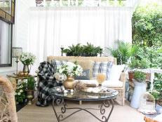 “I designed the foundational elements, such as the wicker sofa, chairs and tables with function and comfort foremost in mind. Those pieces are the “bones” of the look and don’t change,” says Kelly Wilkness of My Soulful Home. “Once you have the foundational ‘bones’ in place layer on the comfort with pillows, throws and maybe an ottoman.”With the furniture in place, Kelly can easily and inexpensively swap out accessories for the seasons. “I used drop cloths that I made into drapes to further delineate the space making it more cozy and room-like,” she says. “Vintage pieces always lend character and a unique quality to a space. On my porch the chippy birdcage and lion statuary fill that role.”