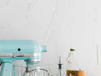 An azure blue stand mixer, bamboo bowls, salt and pepper grinders, and glass oil and vinegar bottles sit on the counter of the kitchen’s baking center.
