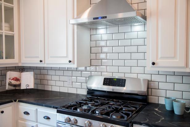 All new white cabinets and black marble countertops bring a modern look to the kitchen.  A new stainless steel range and vent hood is surrounded by a beveled subway tile backsplash, as seen on HGTV's Fixer Upper.  (detail)