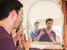 Drew Scott checks himself in the mirror at the existing fireplace structure in the living room at Drew and his fiancé Linda’s soon to be remodeled home, as seen on Property Brothers at Home: Honeymoon House.