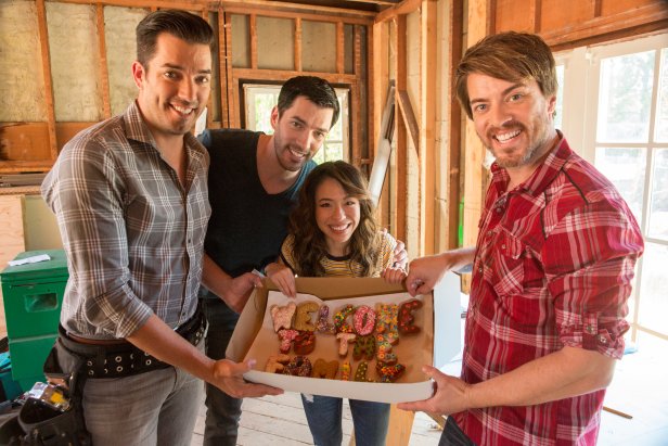 Hosts Jonathan and Drew Scott, Drew's fiancee Linda, and JD Scott show off a box of donughts that spells "Welcome to the the family" brought by JD during construction in Drew's honeymoon house, which is undergoing an extensive remodel ahead of Drew and Linda's upcoming wedding, as seen on Property Brothers at Home: Drew's Honeymoon House.