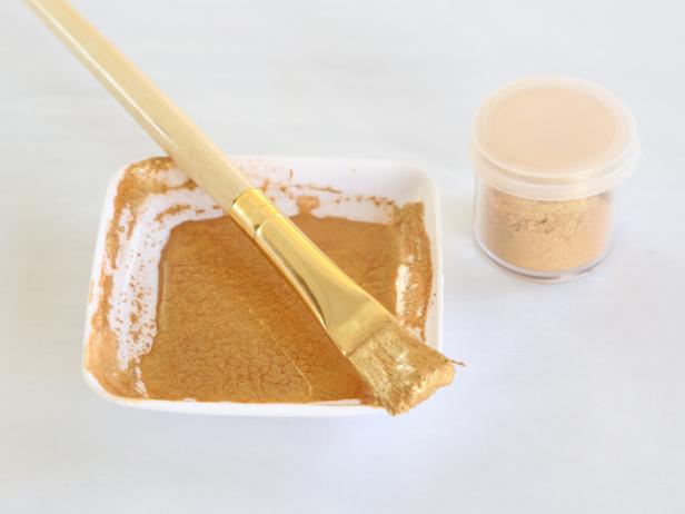Combine gold luster dust and drops of vodka in a small condiment cup and stir until a thin gold paint consistency is achieved.  Load a stiff bristle brush with the paint.