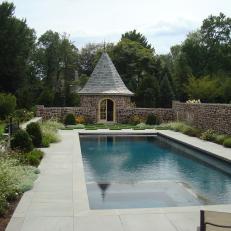Quaint Cottage Backyard Swimming Pool With Surrounding Stone Wall, Planted Border and Small Covered Shed 