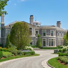 Grand Gray Stone Home Exterior With Gravel Driveway and Lush Planted Front Yard 