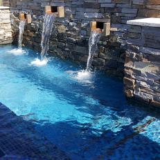 Natural Rock Retaining Wall With Water Feature Flowing Into Swimming Pool With Mosaic Tile Detailing 