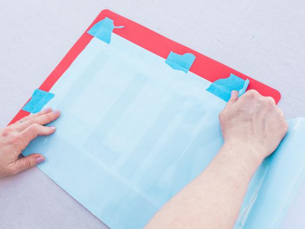 Step 2- Secure Adhesive Over Template
Lay the DIY stencil paper over the printed template. Use painter’s tape to secure them to each other. Be sure to align these so that the sticky side of the stencil paper is facing down (but keep the backing paper on).