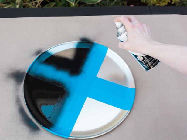 Step 2- Spray Paint X’s
Then spray paint the pans with black spray paint using light, sweeping motions. Allow to dry for 15 minutes. HINT- create a safe “paint area” for this project by placing a drop cloth down on the ground or work surface.
