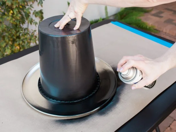 Step 3- Spray Paint O’s
Using an old bucket or bowl with a 10 to 12-inch diameter, create the O’s on the remaining five pizza pans. Spray paint around the bucket’s edge so that you’re left with a silver circle in the middle of the pizza pan.