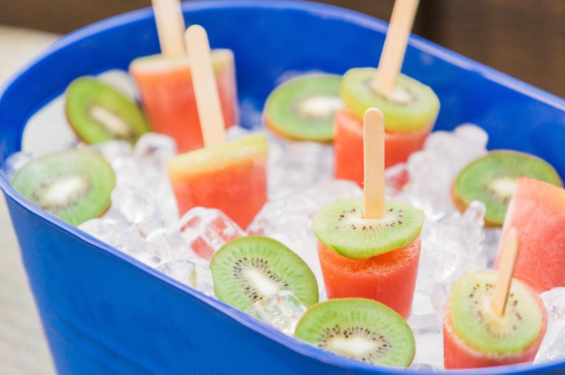 To make these colorful treats blend watermelon chunks, then pulse, strain and pour into small paper cups. Top each cup with a thick slice of kiwi. Place the popsicle stick through the center of the fruit, then freeze. Once frozen, just remove the paper cup and serve! 