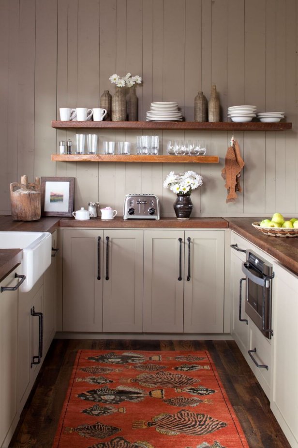 Taupe cabinets are clad in solid wood countertops for the small kitchen in this Montana bunkhouse. Open shelves keep dishes handy, while a vivid orange fish-motif rug adds color to the space.