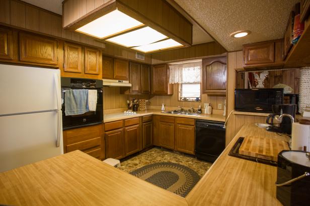The kitchen of Drew Scott's home in Galveston, TX before renovations, as seen on Brother vs Brother. This interior shows very dated, dark wood cabinets and formica counters. (Before #4) 