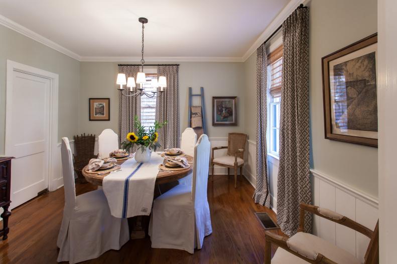 As seen on Home Town, the Carson’s Laurel, MS house had a plain dining room lacking style before renovations by hosts Ben and Erin Napier. After the renovations, the Carson's Laurel, MS dining room now features newly painted gray walls with a white wainscott, updated blinds and drapes, a new china cabinet along with new drop cloth chair covers that host Erin Napier created.  (after)