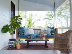 White Covered Porch With Hanging Swing, Wicker Chair and Mixed Blue Throw Pillows