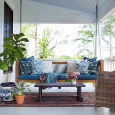 White Covered Porch With Hanging Swing, Wicker Chair and Mixed Blue Throw Pillows