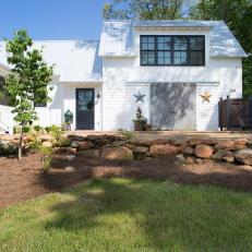 White Farmhouse Exterior With Black Door and Window Frames and Textured Stone Landscaping 