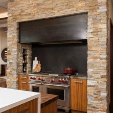 Kitchen Range With Natural Stone Surround, Dark Backsplash and Stainless Steel Appliances