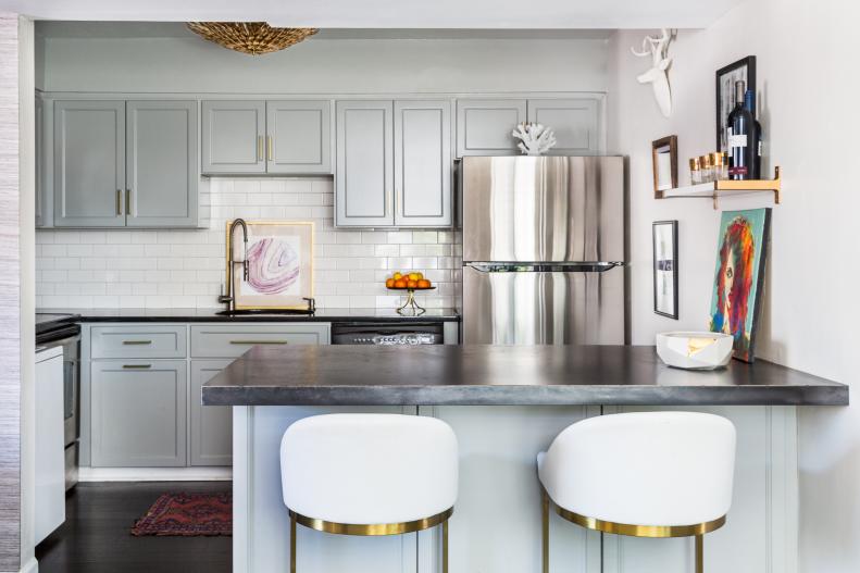 Charming Small Kitchen With Gray-Blue Cabinets The kitchen takes a colorful, industrial turn, showcasing Naomi’s fondness for metallics. The island is topped with an oxidized, steel countertop. The material is a unique twist on the usual granite or marble found in most kitchens. The steel top will patina over time. Its rough-hewn texture is also a pleasing contrast to the stainless steel refrigerator and brass elements in the kitchen. Cabinets in a gray-blue tone contrast with the brass pendant overhead. Naomi discovered the pair of vintage white bar stools and painted the legs gold for a finishing metallic touch.