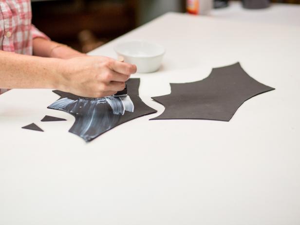 Lay out two sheets of 9x12 black foam sheets together.  Draw an outline of the wings and ears for the bat pumpkins.  Use your scissors to cut along the outline of the wings and ears from the black foam.  While the glue is still wet make sure to pour a significant amount of glitter to fully cover the surface.  Let dry and then carefully shake off the excess glitter.