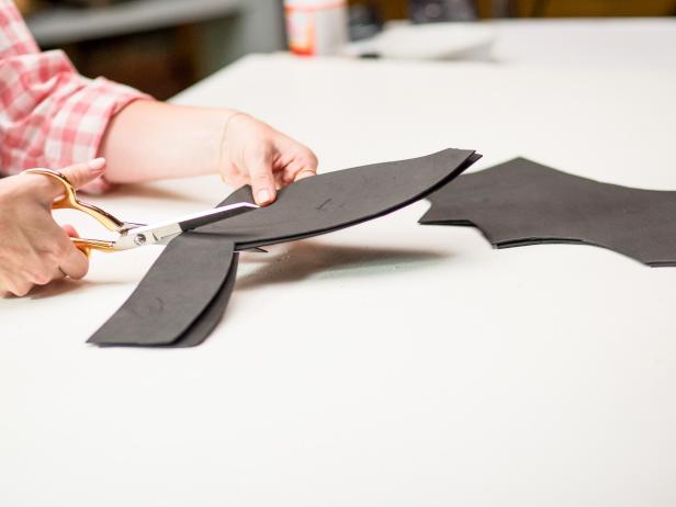 Lay out two sheets of 9x12 black foam sheets together.  Draw an outline of the wings and ears for the bat pumpkins.  Use your scissors to cut along the outline of the wings and ears from the black foam.  While the glue is still wet make sure to pour a significant amount of glitter to fully cover the surface.  Let dry and then carefully shake off the excess glitter.