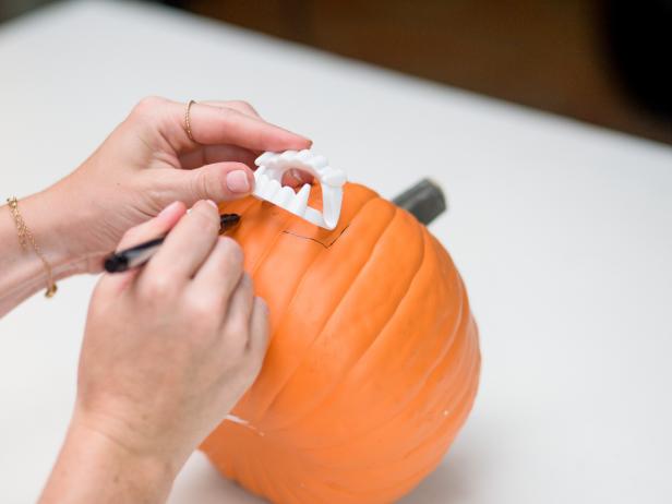 Set the larger pumpkin aside and lay the smaller pumpkin on its side. Trace around the outside of the plastic vampire teeth with a marker near the center of the small faux pumpkin.