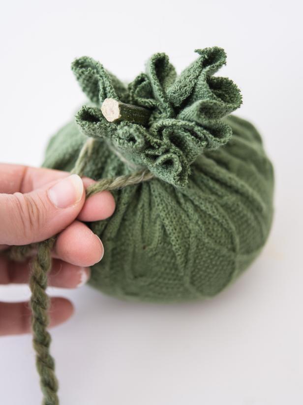 Cut a length of yarn long enough to wrap around pumpkin stem and tie.  Cinch sweater fabric around pumpkin stem and secure tightly with a length of yarn.  Trim yarn tails.