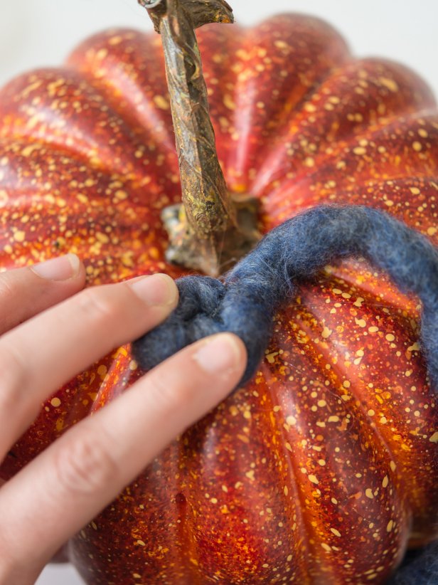 Yarn can be positioned on the pumpkin in a variety of patterns.  In this example, the yarn is wrapped in swirls and âSâ shapes.  Apply hot glue to surface of plastic pumpkin and immediately stick yarn in place.  Hold yarn for 3-5 seconds until glue cools.  When pattern is complete, cut off excess yarn, add a dab of glue to end, and tuck into yarn pattern to hide.  Continue in this manner until pumpkin is completely covered.  Tip: To prevent finger burns from hot glue, use a wooden popsicle stick to hold down yarn as itâs cooling.