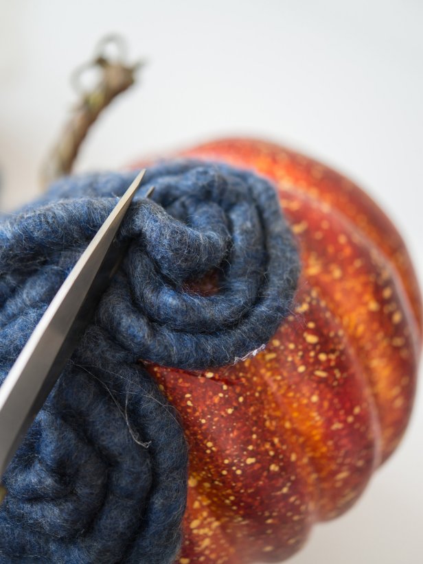 Yarn can be positioned on the pumpkin in a variety of patterns.  In this example, the yarn is wrapped in swirls and âSâ shapes.  Apply hot glue to surface of plastic pumpkin and immediately stick yarn in place.  Hold yarn for 3-5 seconds until glue cools.  When pattern is complete, cut off excess yarn, add a dab of glue to end, and tuck into yarn pattern to hide.  Continue in this manner until pumpkin is completely covered.  Tip: To prevent finger burns from hot glue, use a wooden popsicle stick to hold down yarn as itâs cooling.