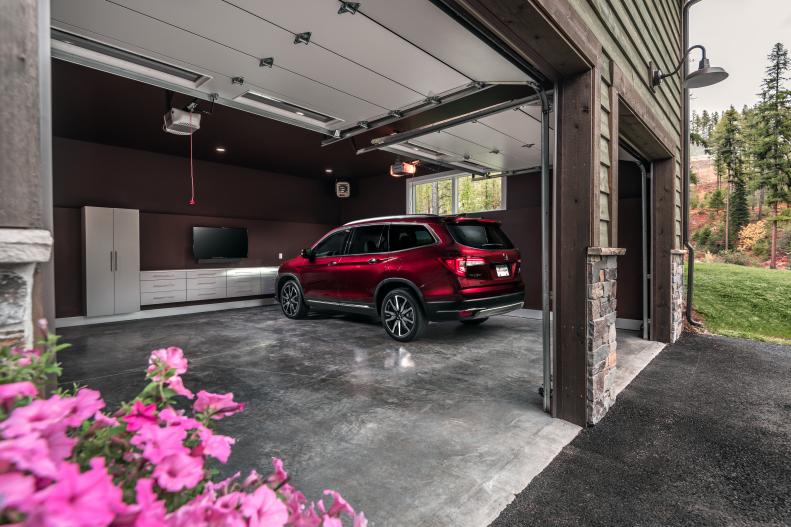 With the front double doors open, this view offers a glimpse inside the spacious and organized heated garage with concrete floor and a ceiling and walls painted a rich dark coffee brown color. This garage and the house both feature an autumn color scheme with hues found in nature. 