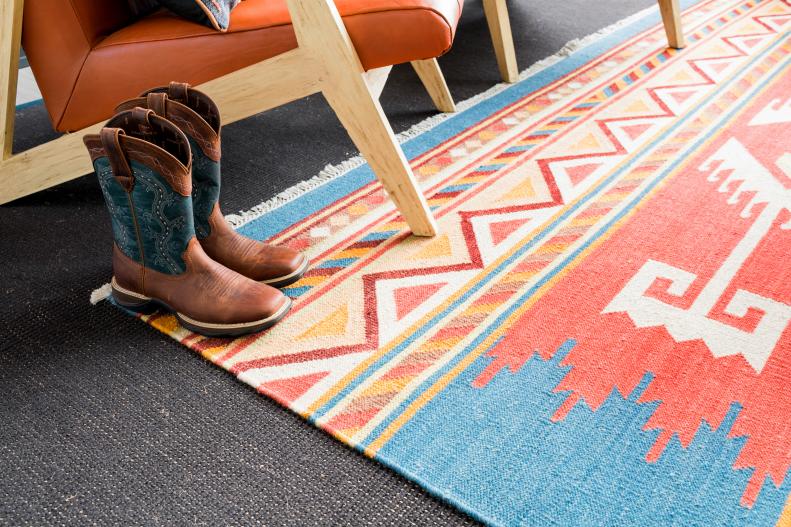 A dark brown, hand-woven sisal area rug with black border was placed under a smaller hand-woven flat weave wool area rug with a Western pattern with blue, orange and rust colors. The rugs add warmth and help delineate the lounge area from surrounding spaces.