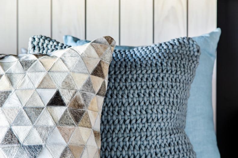 A handmade throw pillow with classic hide construction and a geometric pattern and a woven rope cotton throw pillow in pale ocean blue are two of the pillows that add comfort and color on top of the bed.