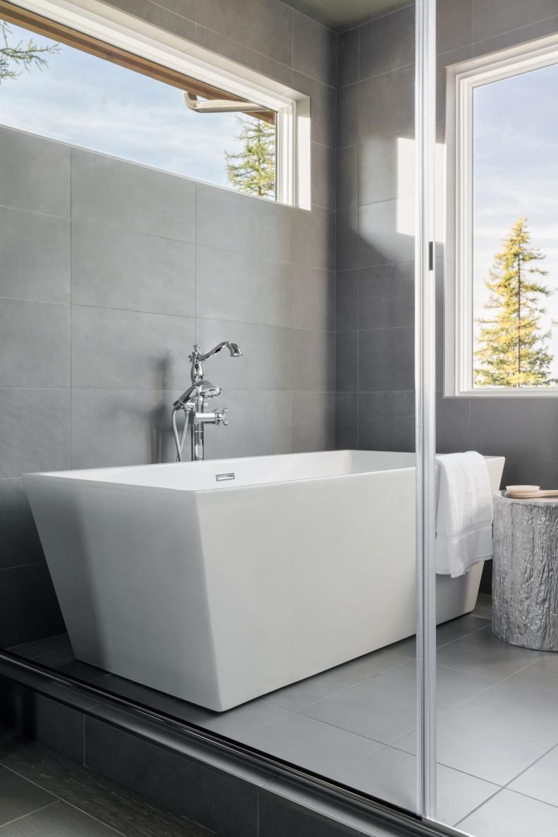 A contemporary tub in classic white with a traditional-style faucet in silver pop against the gray tiled bath area.