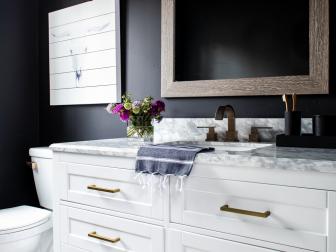 The powder room’s freestanding white vanity has a rustic wood framed mirror and 3-light vanity light for illumination above. Sophisticated black walls with a subtle softness provide a dramatic backdrop and add moody style to this chic space with a Western flavor. 