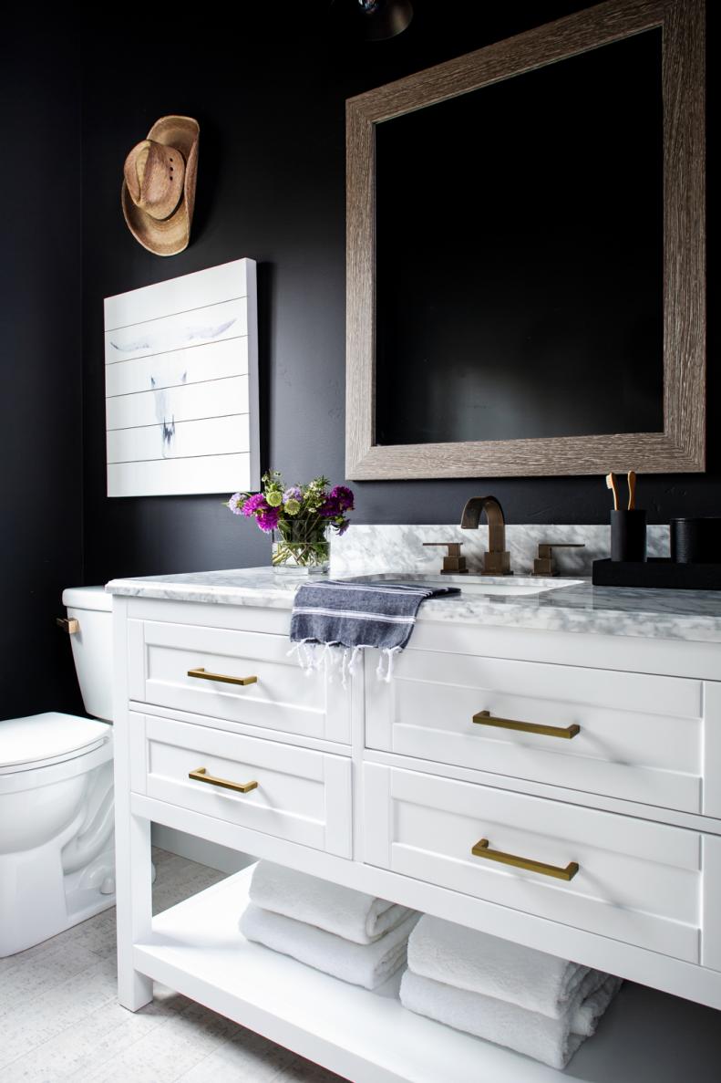 The powder room’s freestanding white vanity has a rustic wood framed mirror and 3-light vanity light for illumination above. Sophisticated black walls with a subtle softness provide a dramatic backdrop and add moody style to this chic space with a Western flavor. 