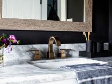 The vanity's beautiful Carrera marble countertop picks up the black and white design details in the powder room, and coordinates with the matte champagne bronze finish on the sink faucet. 